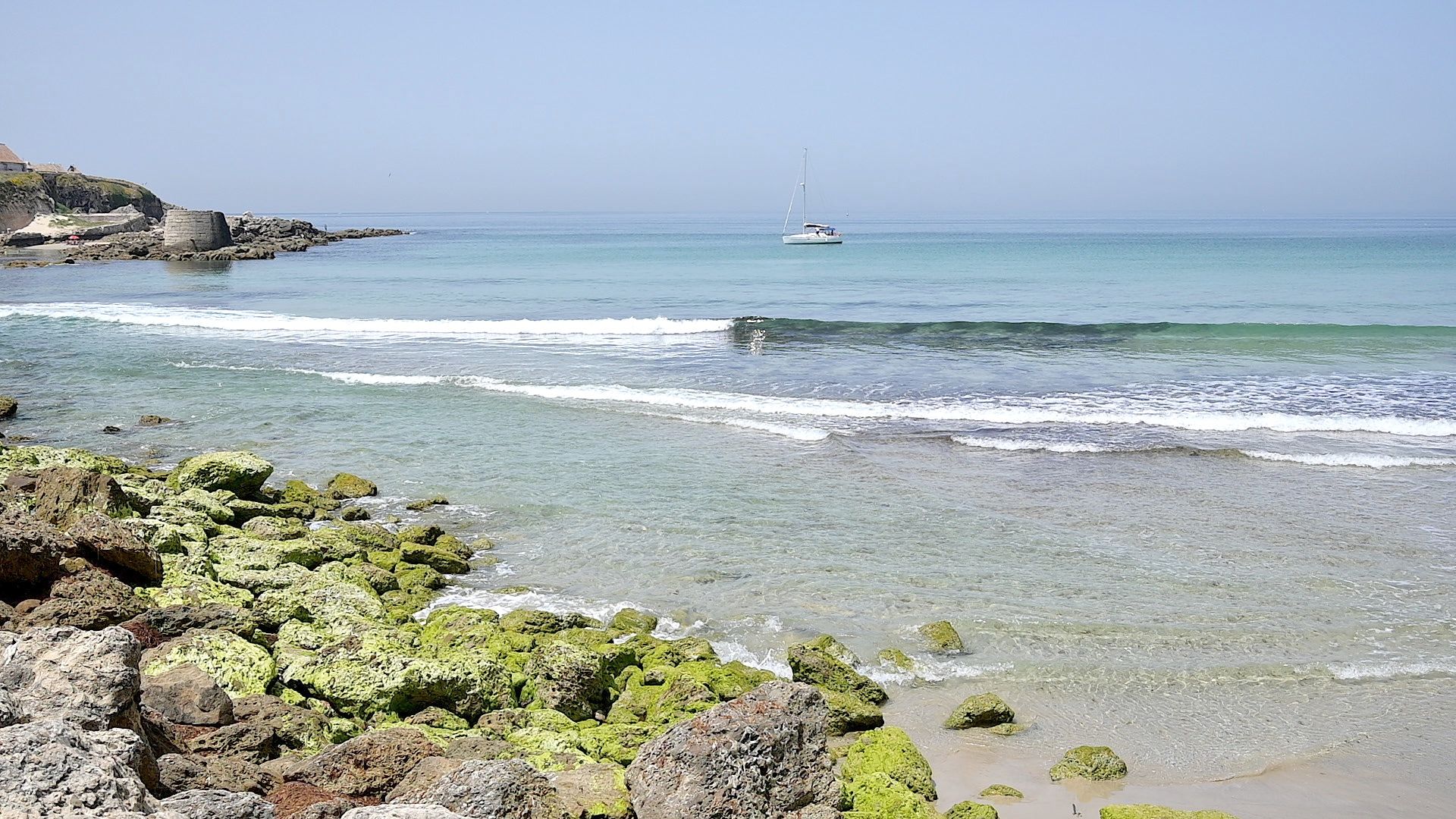 Cala de arena junto al casco antiguo de Tarifa con un velero fondeado en aguas transparentes
