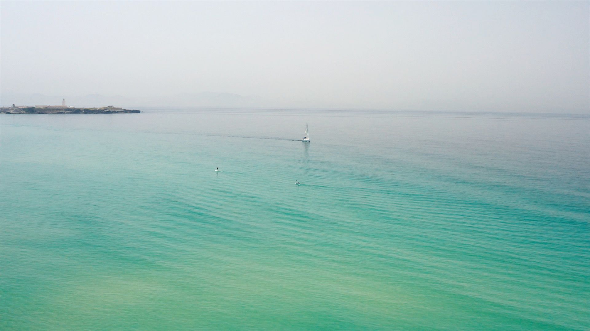 Vista aérea del mar turquesa de Tarifa con un velero y dos paddle surfistas