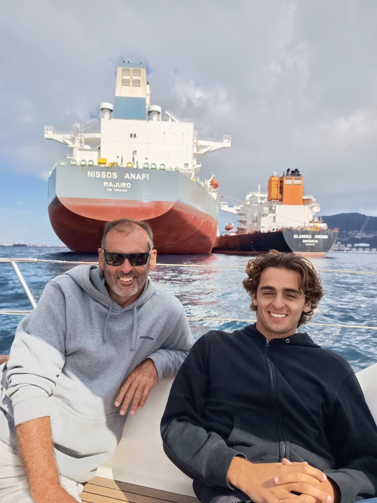 Two guests smiling on deck with the big cargo ships of the Strait of Gibraltar and the Rock behind