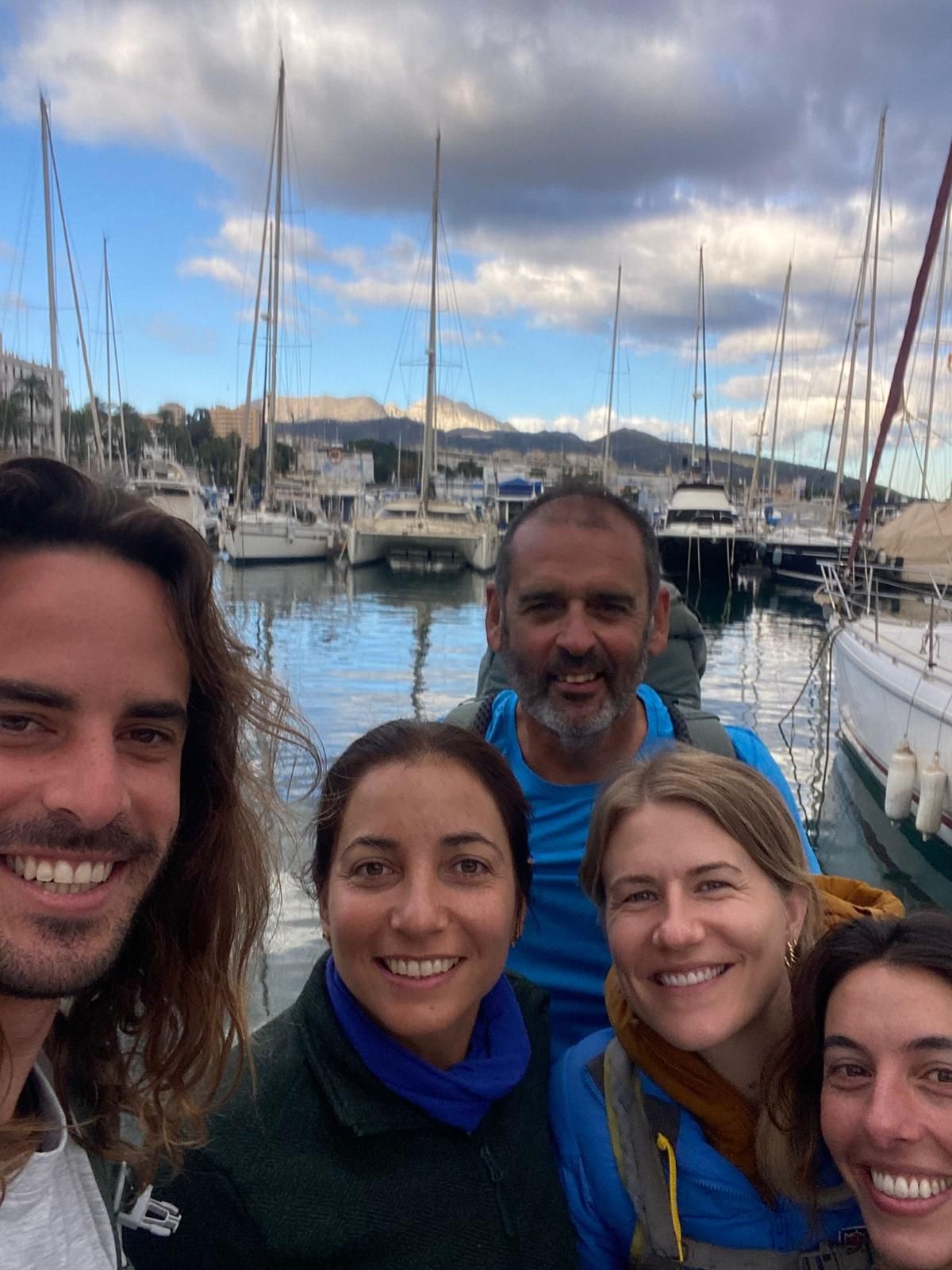 A group of guests and the skipper pose for a selfie at Tarifa marina at golden hour