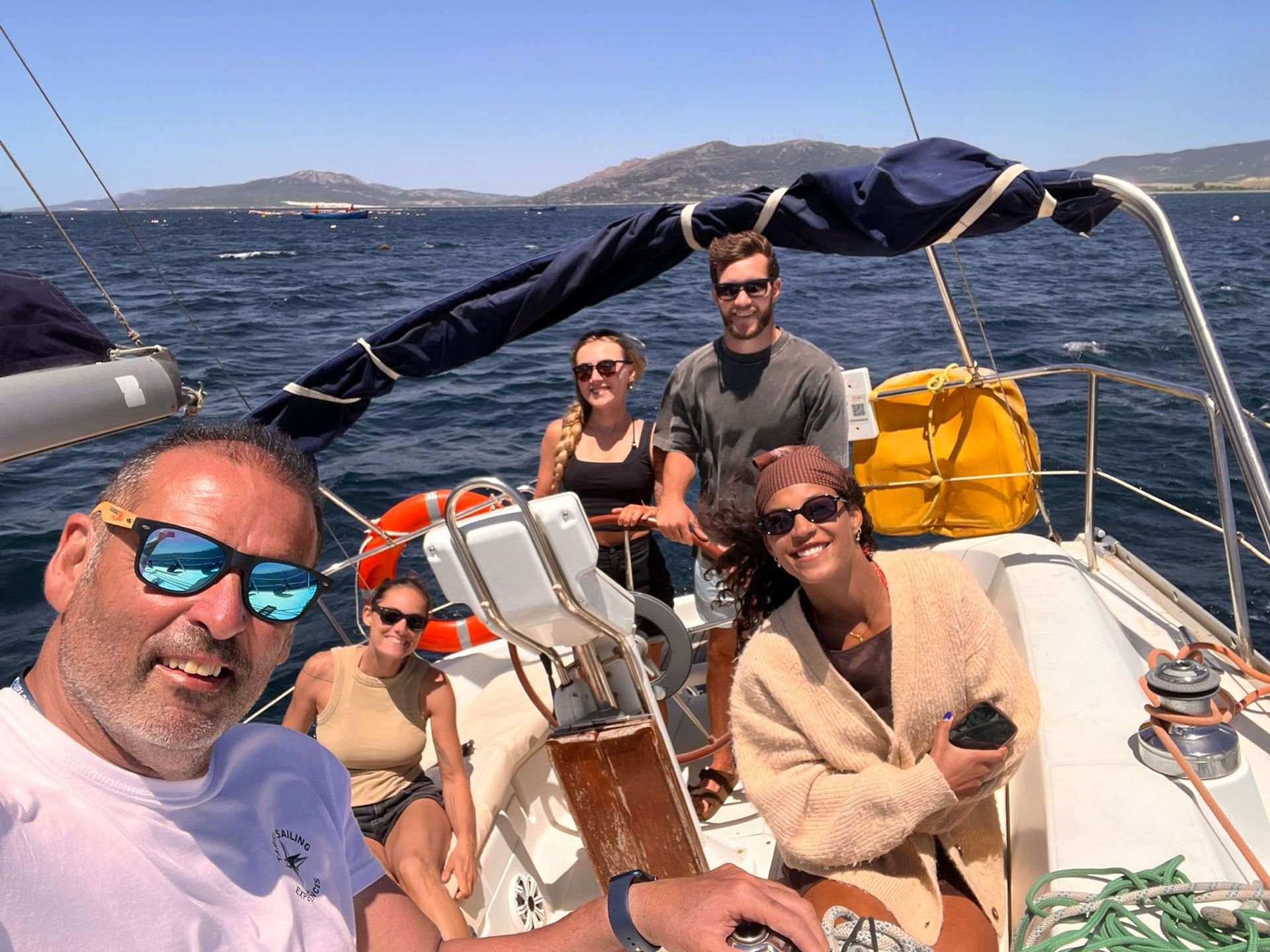 El patrón y un grupo de pasajeros al timón un día soleado navegando por el Estrecho de Gibraltar, con las montañas al fondo