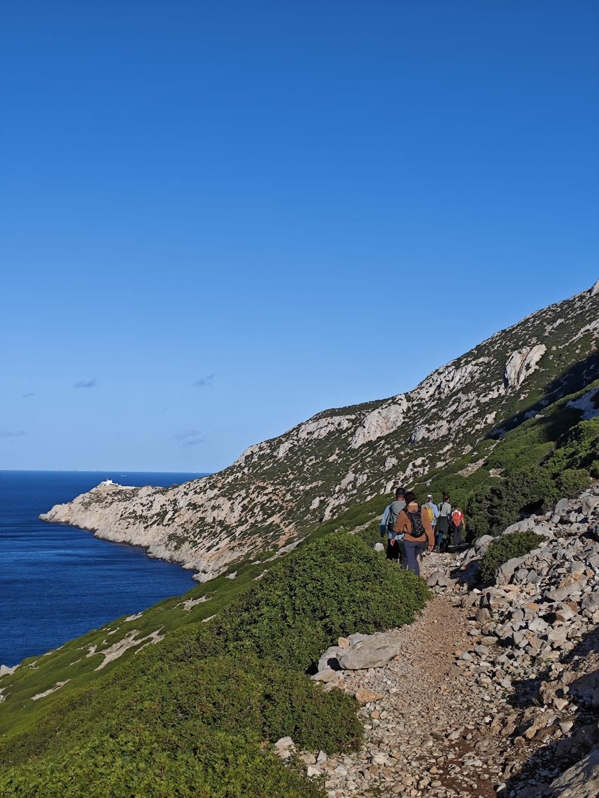 Excursionistas recorriendo el sendero costero rocoso del Jebel Musa sobre el Mediterráneo